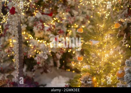 Spielzeugvögel sitzen auf einem Baum mit Lichtern. Weihnachtsinstallation. Hohe Qualität Stockfoto