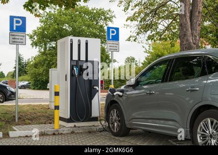 Ein Auto an einer Ladestation und auf dem Parkschild befindet sich das Zusatzschild mit dem deutschen Text „Elektrofahrzeuge während des Ladevorgangs“ Stockfoto