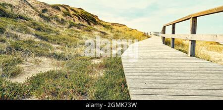 Eine hölzerne Promenade an einer erhöhten grasbewachsenen Küste unter einem bewölkten Himmel Stockfoto