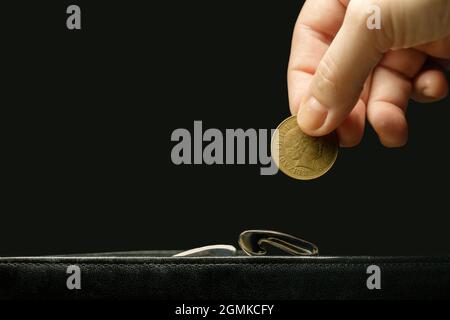 Die Hand einer unsichtbaren Frau legt eine Münze in eine Brieftasche Stockfoto