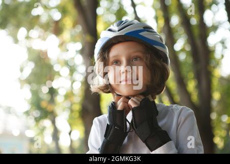 Netter Junge, der Schutzhelm für das Skaten im Park aufsetzt Stockfoto