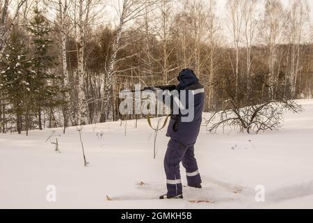 Ein Jäger oder Wilderer steht auf Skiern am Waldrand und zielt mit seiner Waffe auf Beute Stockfoto