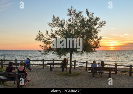Menschen sitzen auf Bänken am Meer bewundern den Sonnenuntergang im Sommer, San Vincenzo, Livorno, Toskana, Italien Stockfoto