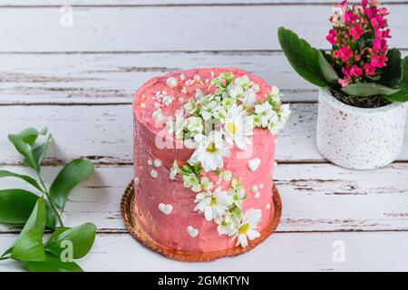 Schokoladenkuchen mit rosa Buttercreme bedeckt. Verziert mit weißen Herzen, Perlen und Blumen. Stockfoto