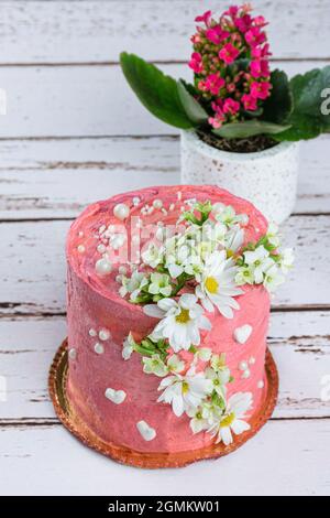 Schokoladenkuchen mit rosa Buttercreme bedeckt. Verziert mit weißen Herzen, Perlen und Blumen (vertikales Foto). Stockfoto