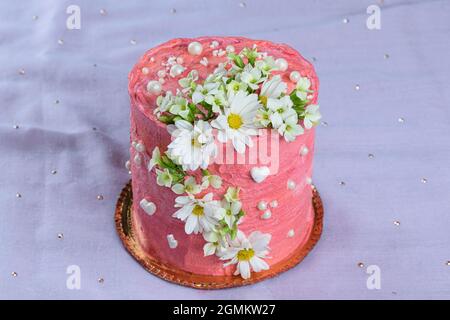 Schokoladenkuchen mit rosa Buttercreme bedeckt. Verziert mit weißen Herzen, Perlen und Blumen. Auf einem violetten Stoff. Stockfoto