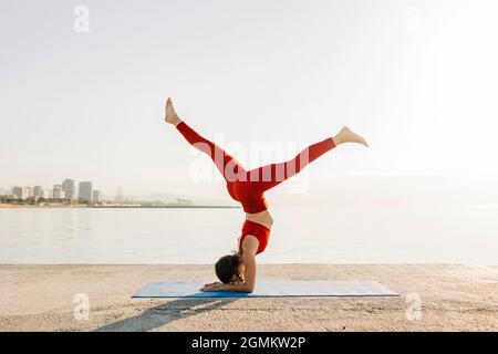 Athletische junge hispanische Frau in roter Sportkleidung, die morgens Yoga macht Stockfoto