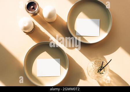Leere Papierblattkarten mockup auf beigem Hintergrund in Sonnenlicht. Keramikplatten und Kerzen, Duftstäbchen in Glasvase mit langen Schatten. Draufsicht Stockfoto