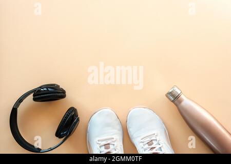 Weiße Sneaker, Kopfhörer und Flasche mit Wasser auf pastellorangefarbenem Hintergrund. Konzept für gesundes Leben, Sport und Training. Flach liegend, Draufsicht, Kopie Stockfoto