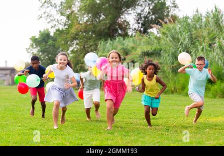 Fröhliche Jugendliche Jungen und Mädchen mit Luftballons auf grünem Rasen Stockfoto