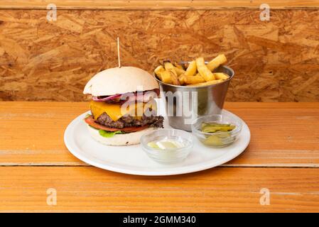 Rinderburger mit 250 Gramm Fleisch, roten Zwiebeln, Tomatenscheiben, Eisbergsalat, geräuchertem Speck, cheddar-Käse, eingelegte Gurken und Pommes frites Stockfoto