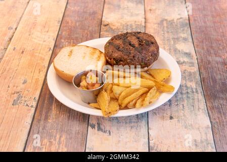 Auf Holztisch gegrillter Rindfleisch-Burger mit Pico de gallo und Keilchips Stockfoto