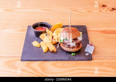 Kleiner kobe-Rindfleisch-Burger mit geschnittenem Manchego-Käse, karamellisierten Zwiebeln und Keilfries Stockfoto