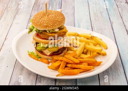 Spektakulärer Double-Decker-Burger mit knusprigem Rindfleisch und Huhn, Salat und Gurken, Senf und Tomaten, geschmolzenem emmental- und Cheddar-Käse und Beilage Stockfoto