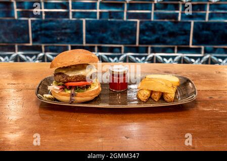 Rindfleisch-Burger mit geschmolzenem Emmentaler-Käse, Salat, Tomaten, Zwiebeln. Tomatenmarmelade und Pommes frites keil Stockfoto