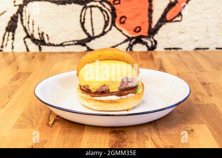 Rindfleisch-Burger mit geschmolzenem Cheddar-Käse, Kumato-Tomaten, Mayonnaise, Brioche-Brot, weißem Teller und Salat Stockfoto