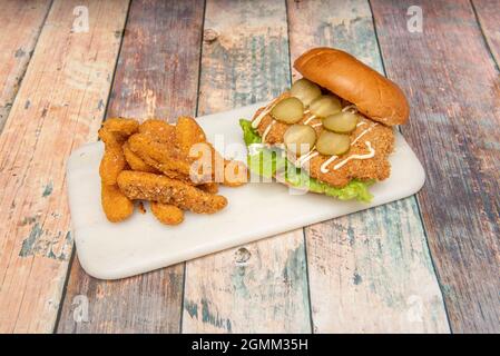 Knuspriger Chicken Burger mit Gurken, Mayonnaise und Salat mit zerschlackten Mozzarella-Käsefingern Stockfoto