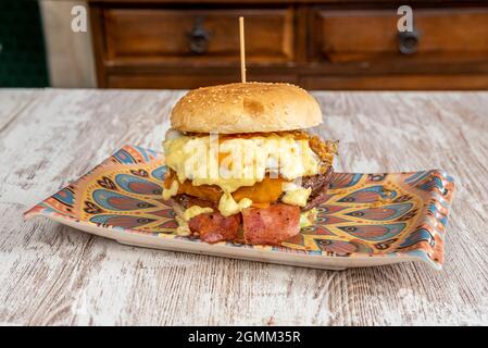 Rinderburger mit geschmolzenem Käse verschiedener Geschmacksrichtungen, Spiegelei, gebratenem geräuchertem Speck, Salat und knuspriger Zwiebel Stockfoto