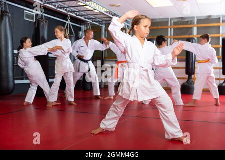 Weibliche Karate-Kämpferin im weißen Kimono, Kampfstellung. Kinder zu zweit üben Karate Stockfoto