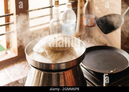 Idli oder untätig, herzhafter Reiskuchen aus Indien, Frühstücksspeisen im Süden. Frau, die zu Hause kocht, warme Speisen mit Dampf Stockfoto