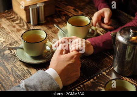 Junges Paar, das bei kaltem Wetter Tee trinkt und sich in einem Café die Hände hält. Stockfoto