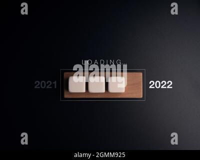 Verladung von 2021 auf das 2022-Jahres-Konzept. Wort- und weiße Würfel-Blöcke auf der hölzernen Fortschrittsleiste, dunkler Hintergrund. Man ist auf der Arbeit, um etwas zu aktualisieren Stockfoto