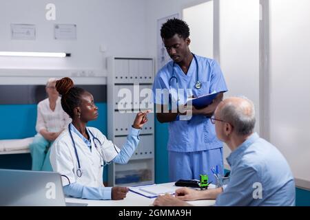 Professionelle medizinische Team von schwarzen Menschen, die Beratung mit älteren Patienten in der Klinik. afroamerikanischer Arzt und Krankenschwester im Gespräch mit älteren kaukasischen Menschen am Schreibtisch Stockfoto