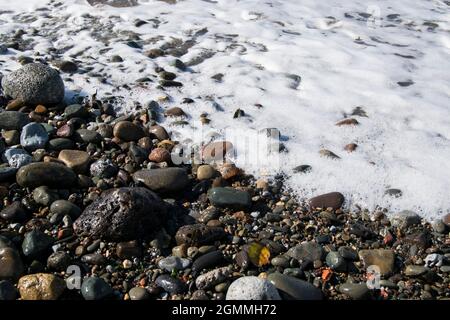 Weißwasserschaumstoff am Kiesstrand von Maryport in Cumbria Stockfoto