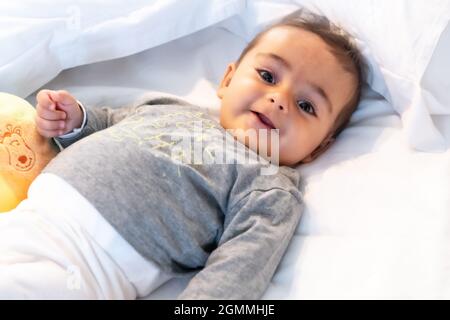 Ich wachte gerade auf entzückendes 5 Monate altes kaukasisches Baby lächelnd in einem grauen T-Shirt und einem Ball zum Spielen Stockfoto