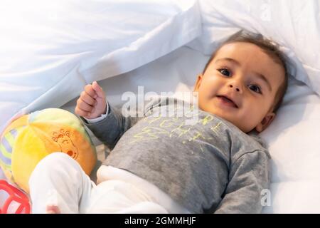 Ich wachte gerade auf entzückendes 5 Monate altes kaukasisches Baby lächelnd in einem grauen T-Shirt und einem Ball zum Spielen Stockfoto