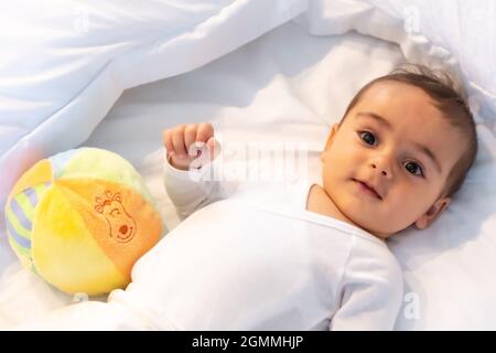 Ich wachte gerade auf entzückendes 5 Monate altes kaukasisches Baby lächelnd in einem grauen T-Shirt und einem Ball zum Spielen Stockfoto