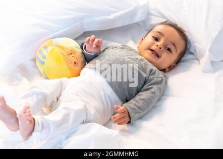 Ich wachte gerade auf entzückendes 5 Monate altes kaukasisches Baby lächelnd in einem grauen T-Shirt und einem Ball zum Spielen Stockfoto