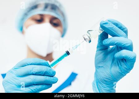 Eine Ärztin mit einer medizinischen Gesichtsmaske und Handschuhen wählt den Impfstoff aus einer Ampulle in eine Spritze. Nahaufnahme des Arztes. Impfung gegen Infektionskrankheiten und Erkältungen. Stockfoto