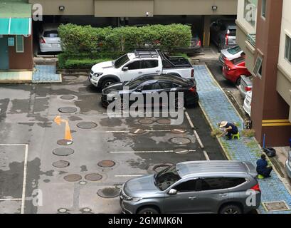 Bangkok, Thailand - 20. September 2021 : Eine Arbeiterin nutzt einen Schneider, um Unkraut zu beseitigen, das auf dem Bürgersteig auf dem Parkplatz überwuchert ist Stockfoto