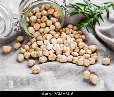 Ungekochte getrocknete Kichererbsen im Glas auf grauem Textilhintergrund Stockfoto