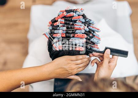 Hände eines Friseurs, der das Haar eines Mannes mit Lockenwicklern mithilfe eines Kamms fixiert Stockfoto