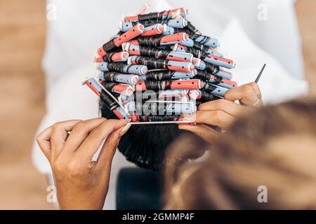 Hände eines Friseurs, der die Haare eines Mannes mit Lockenwicklern fixiert Stockfoto