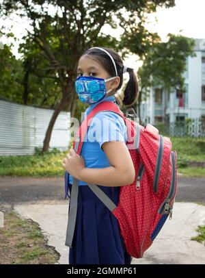 Porträt eines glücklichen indischen Mädchen Schüler in blauer Schuluniform mit roter Tasche und Nasenmaske Schutz zur Schule gehen Stockfoto