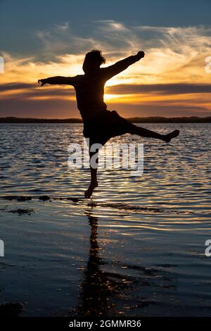 Silhouette Junge springen in Meeresbrandung bei Sonnenuntergang Stockfoto