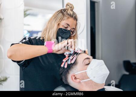 Friseur Curling das Haar eines Mannes mit einer Maske Stockfoto