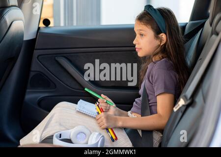Nettes kleines Mädchen mit Wachsmalstiften warten Eltern, während sie auf dem Rücksitz des Autos sitzen Stockfoto