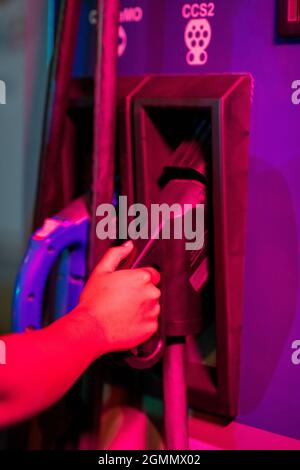 Hand einer jungen Frau, die Pumpe zum Laden eines Elektroautos an der Station nimmt Stockfoto