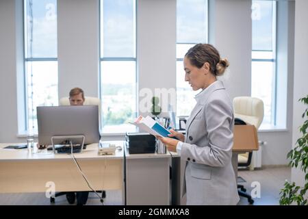 Seitenansicht einer jungen Geschäftsfrau in grauem Anzug, die im Büro durch die Papiere schaute Stockfoto