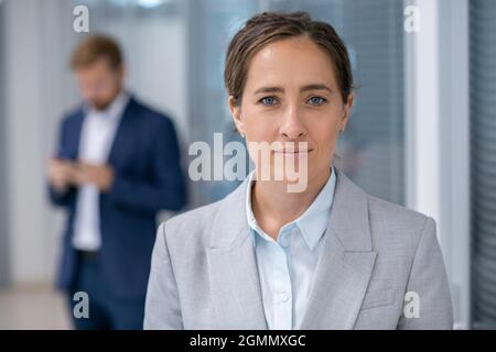 Junge, selbstbewusste Geschäftsführerin in grauer Formkleidung, die gegen ihre Kollegin steht Stockfoto