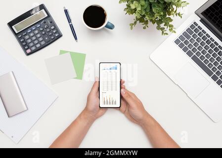 Analyst arbeitet mit den Daten. Grafiken auf dem Smartphone-Bildschirm, flache Lay-Komposition Stockfoto
