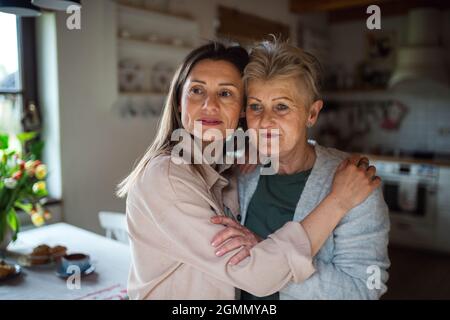Porträt einer älteren Mutter, die sich zuhause mit der erwachsenen Tochter umarmt und zur Seite schaut. Stockfoto