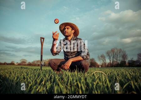 Gemischter männlicher Bauer, der auf Weizenfeldern steht und mit Apfel spielt Stockfoto