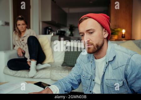 Kaukasischer Mann, der von zu Hause aus mit einer Freundin im Hintergrund arbeitet Stockfoto