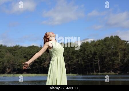 Aufgeregte Frau in grünem Kleid, die die Arme in einem See in die Luft schreit Stockfoto