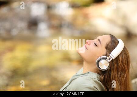 Profil einer entspannten Frau, die frische Luft atmet und Musik am Flussufer hört Stockfoto